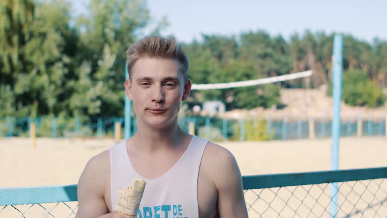 un hombre guapo comiendo shaurma en una cancha de voleibol