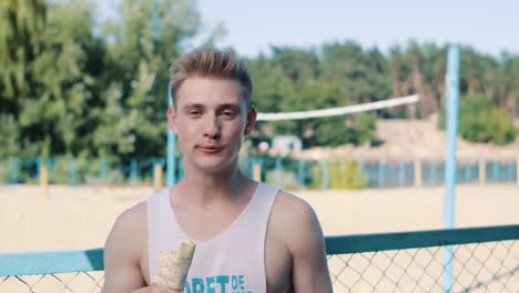 close up of handsome man eating shaurma on a volleyball court