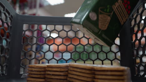 view of a lady in a black coat wearing a backpack placing a juice into a shopping trolley that already contains a pack of biscuits. shot with a handheld camera