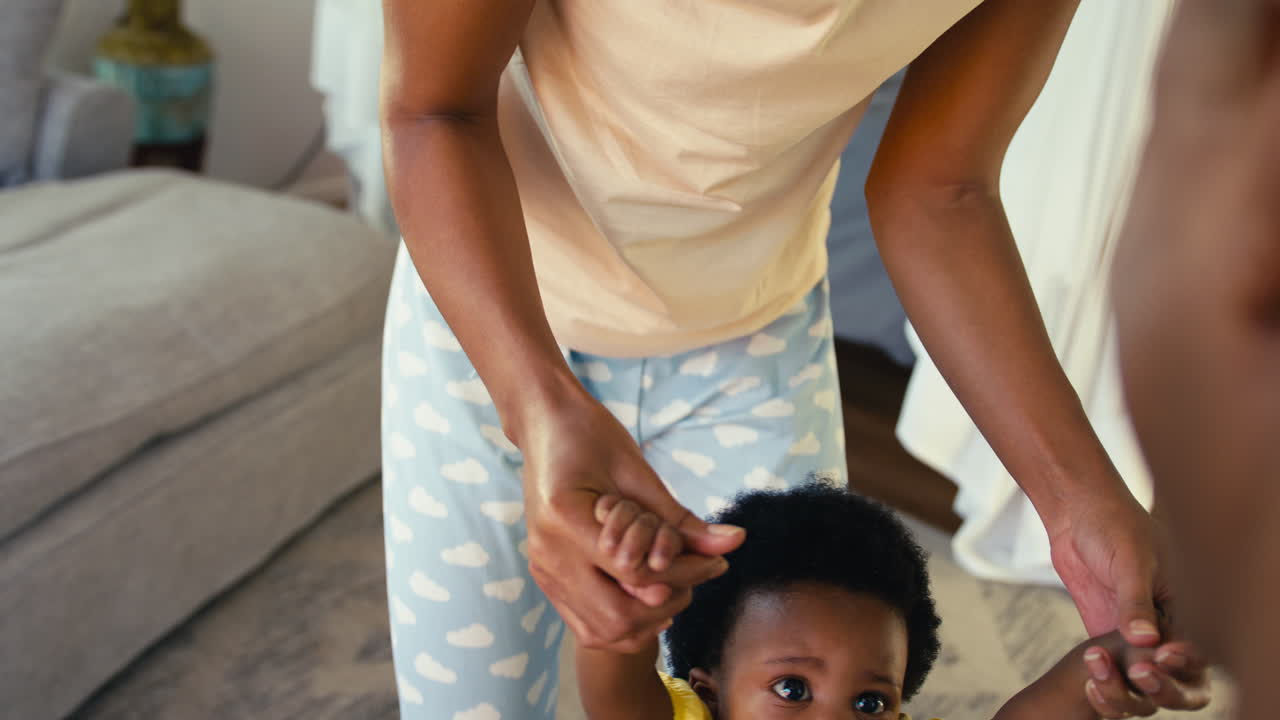 Family Shot As Parents Wearing Pyjamas Help Young Daughter To Walk Indoors At Home