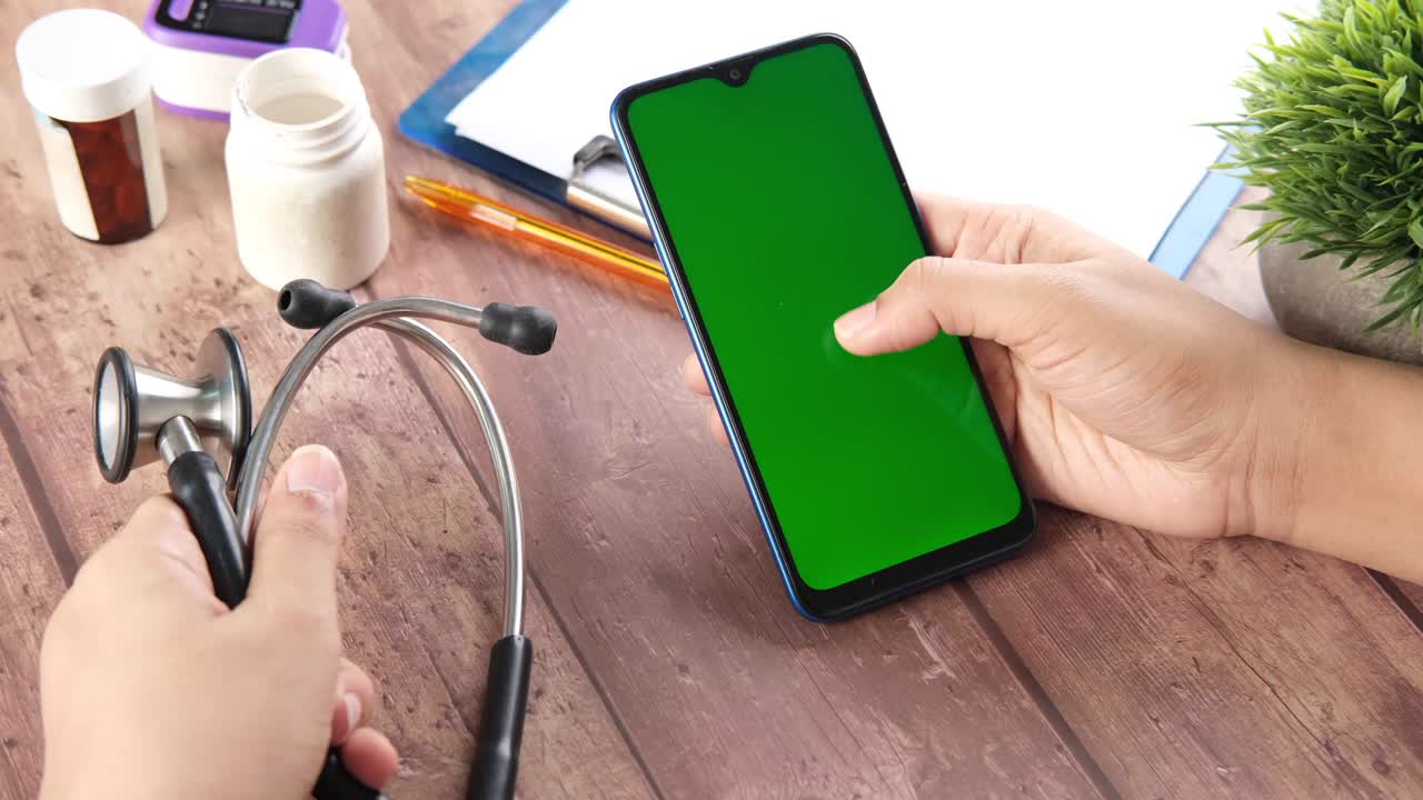 mano del médico sosteniendo un teléfono inteligente con pantalla en blanco en el escritorio de la clínica