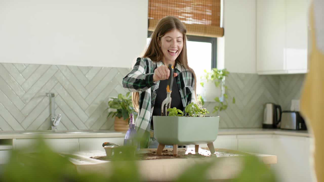 Женщина работает за кухонным столом, расставляет зеленые кашпо, рыхлит почву и указывает за кадр, чтобы показать.