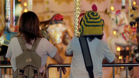 rearview of two friends exploring carnival carousel as they talk and point after school