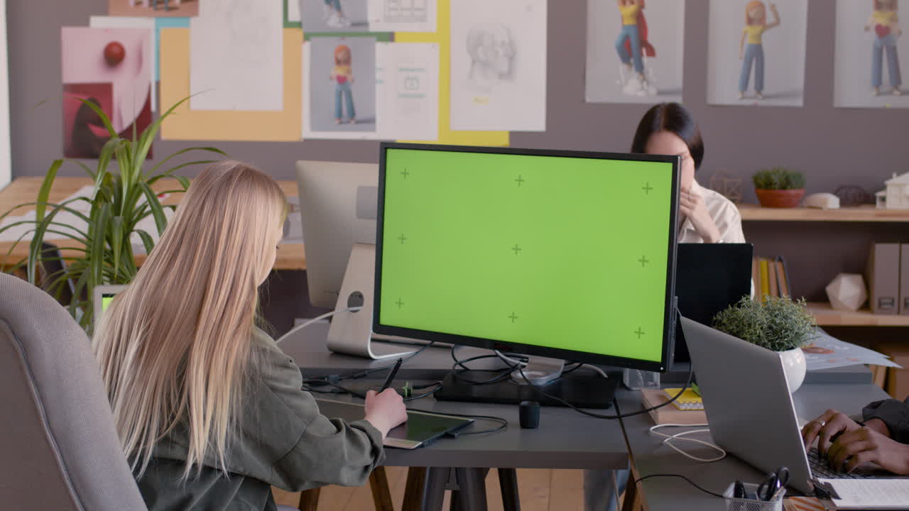diseñadora gráfica femenina usando tableta de dibujo digital y mirando el monitor con pantalla verde en un estudio de animación