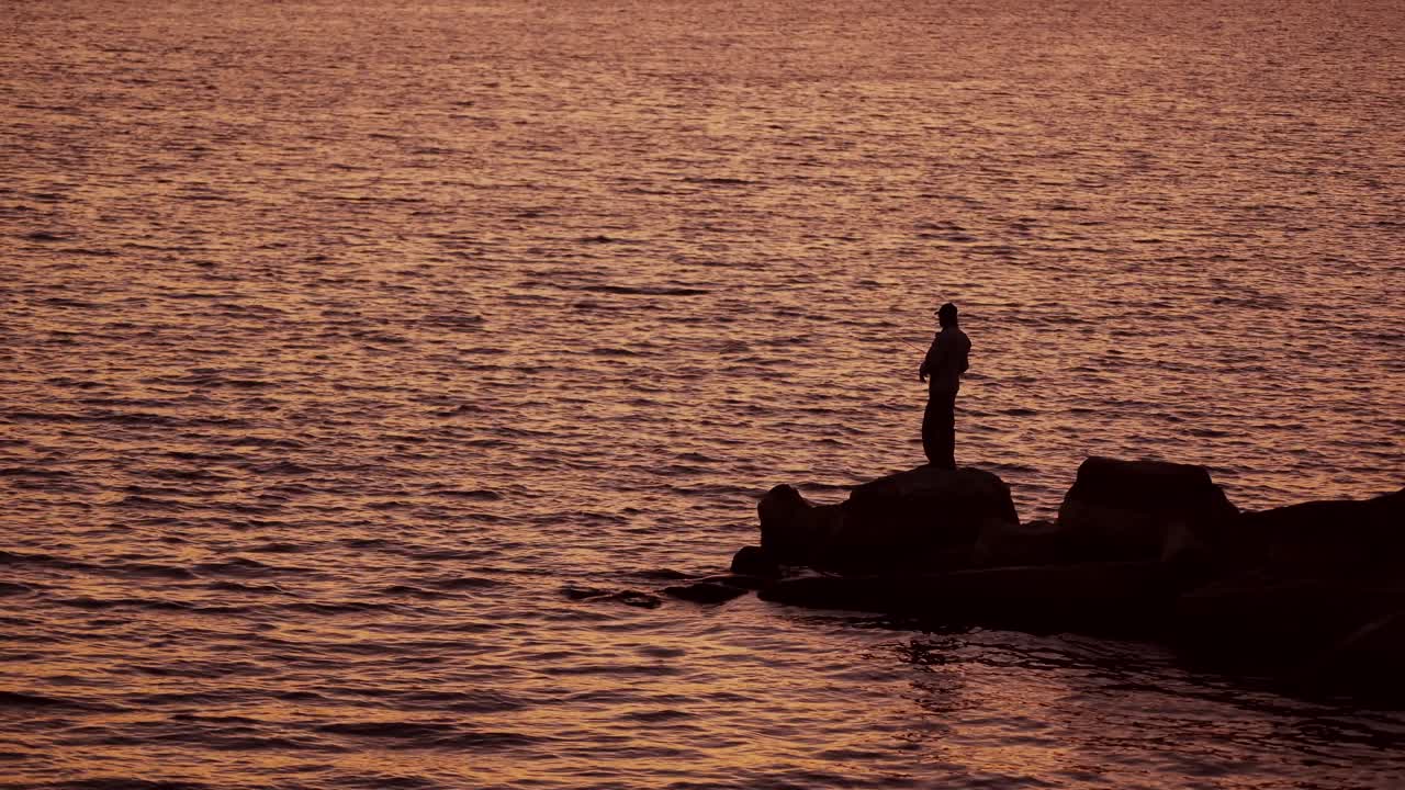 Fishermen on the rocks. Man's silhouette fishing at sunset. Freshwater fishing, catch of fish.