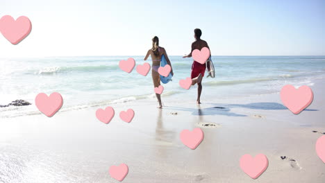 animation of pink hearts over diverse couple running with surfboards on beach