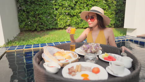 Attractive-Asian-woman-in-swimsuit-having-breakfast-in-private-pool