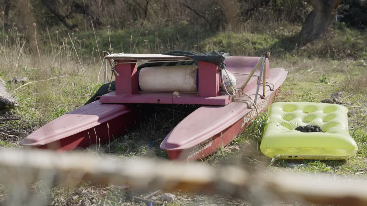 catamarán rojo abandonado a la izquierda con un colchón de aire amarillo al lado en la naturaleza de sabaudia en italia en un día soleado