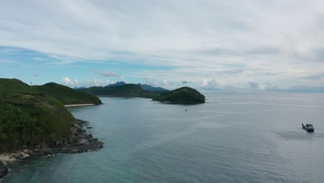 Helicopter-flying-away-from-barge-to-island-with-loaded-bag-of-supplies,-Fiji