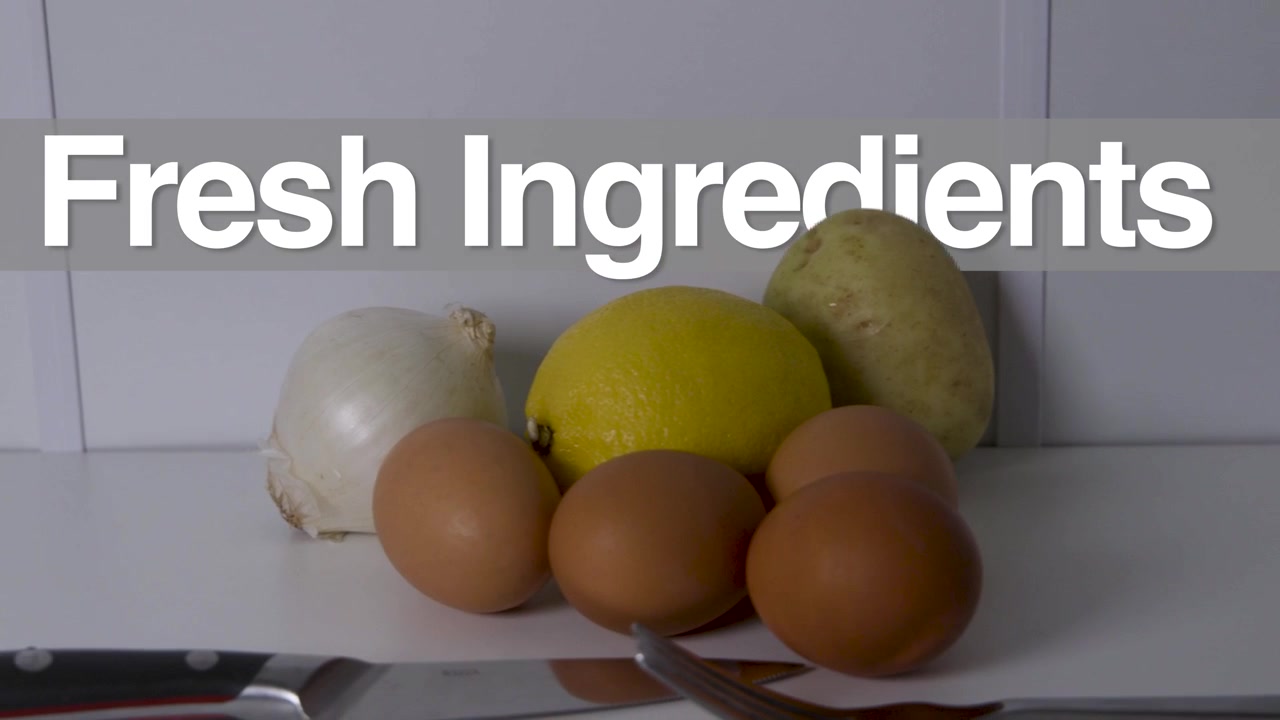 Titlen "Friske Ingredienser" vises over æg, citron, løg, kartoffel og en kokkekniv arrangeret på en ren hvid overflade.