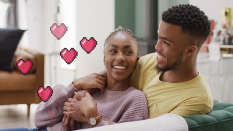 animation of hearts over happy diverse couple on sofa at home