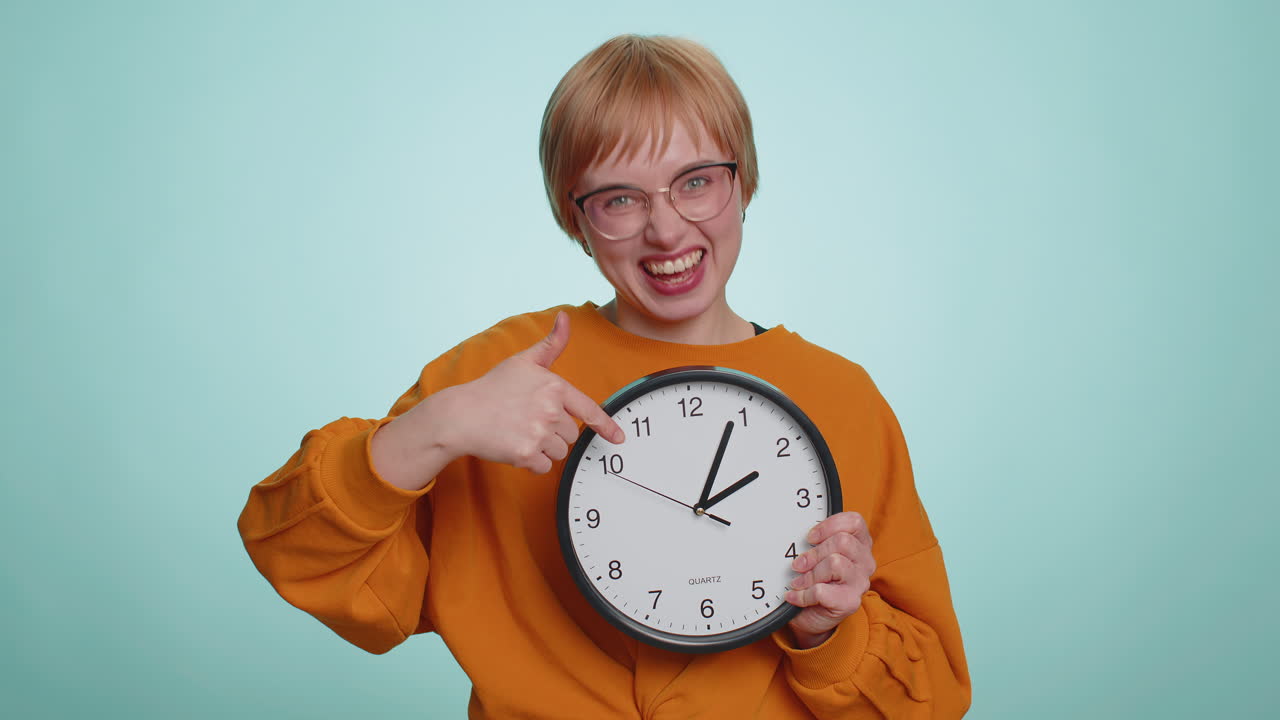 Woman showing time on wall office clock ok thumb up approve pointing finger at camera your time