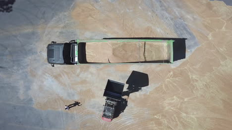 bird's eye view or topdown view on red forklift filling harvested wheat into truck 4k