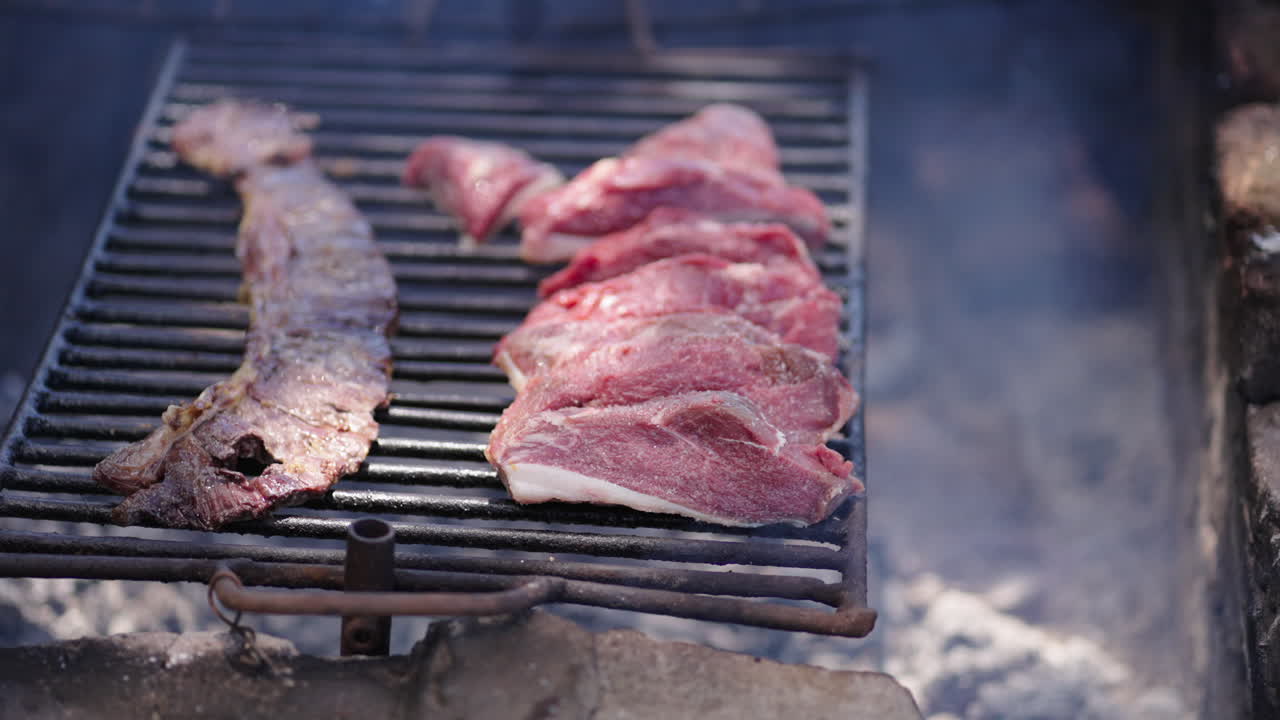 Close up of traditional Argentine asado with skirt steak (entraña) and top sirloin cap (picaña) cooking on metal grill over wood embers, static real time shot, rustic barbecue scene, natural daylight