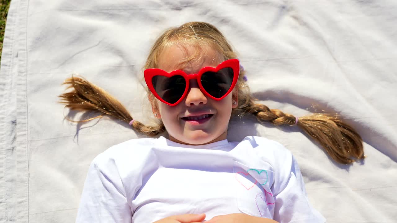 Girl with heart-shaped sunglasses lying on a picnic blanket