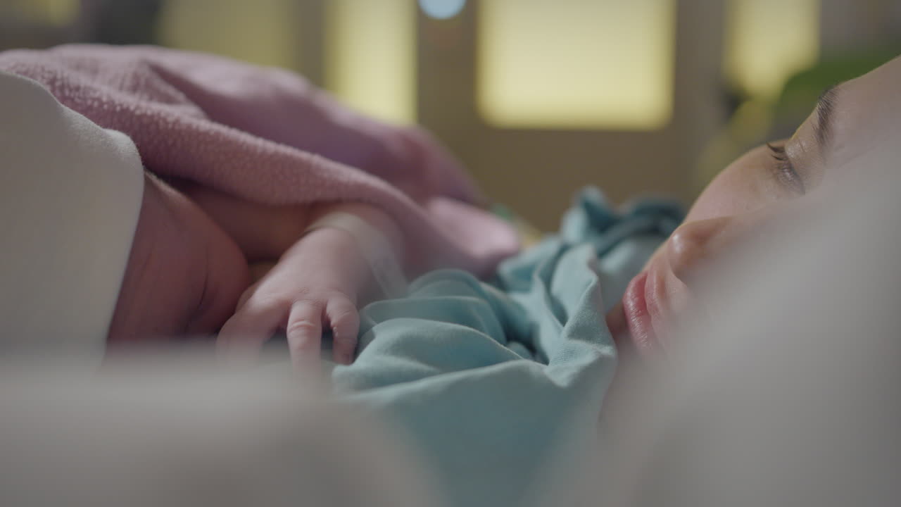 Newborn baby lying next to mother resting in bed. Close up portrait