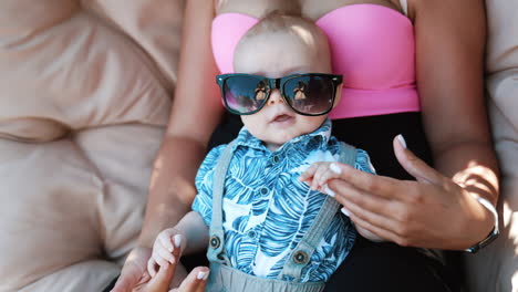 adorable baby boy lying on mom's belly face up. little child wearing mom's sunglasses looking cute. close up.