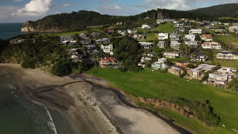 Modern-holiday-houses-properties-at-Langs-Beach,-aerial-pull-back,-sandy-beach,-forested-hills