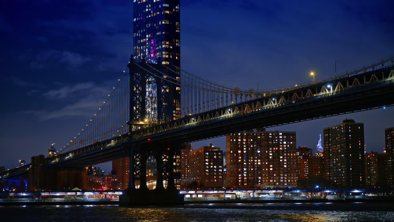 Struttura del Ponte di Manhattan ed edifici cittadini di notte. Veduta dettagliata della costruzione in acciaio del Ponte di Manhattan con edifici residenziali illuminati e grattacieli.