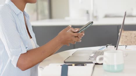 mujer afroamericana sentada en una mesa usando un teléfono inteligente y una computadora portátil, cámara lenta