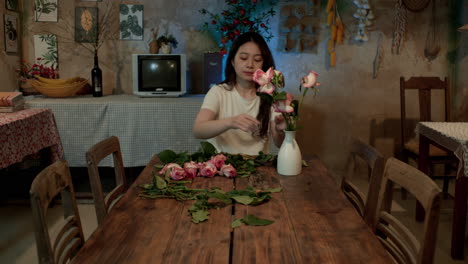 young woman arranges flowers into a vase at a kitchen table