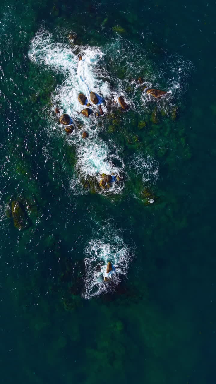 Waves crashing over rocky outcrops in vibrant blue waters during a sunny day, showcasing nature's beauty and tranquility in a coastal paradise