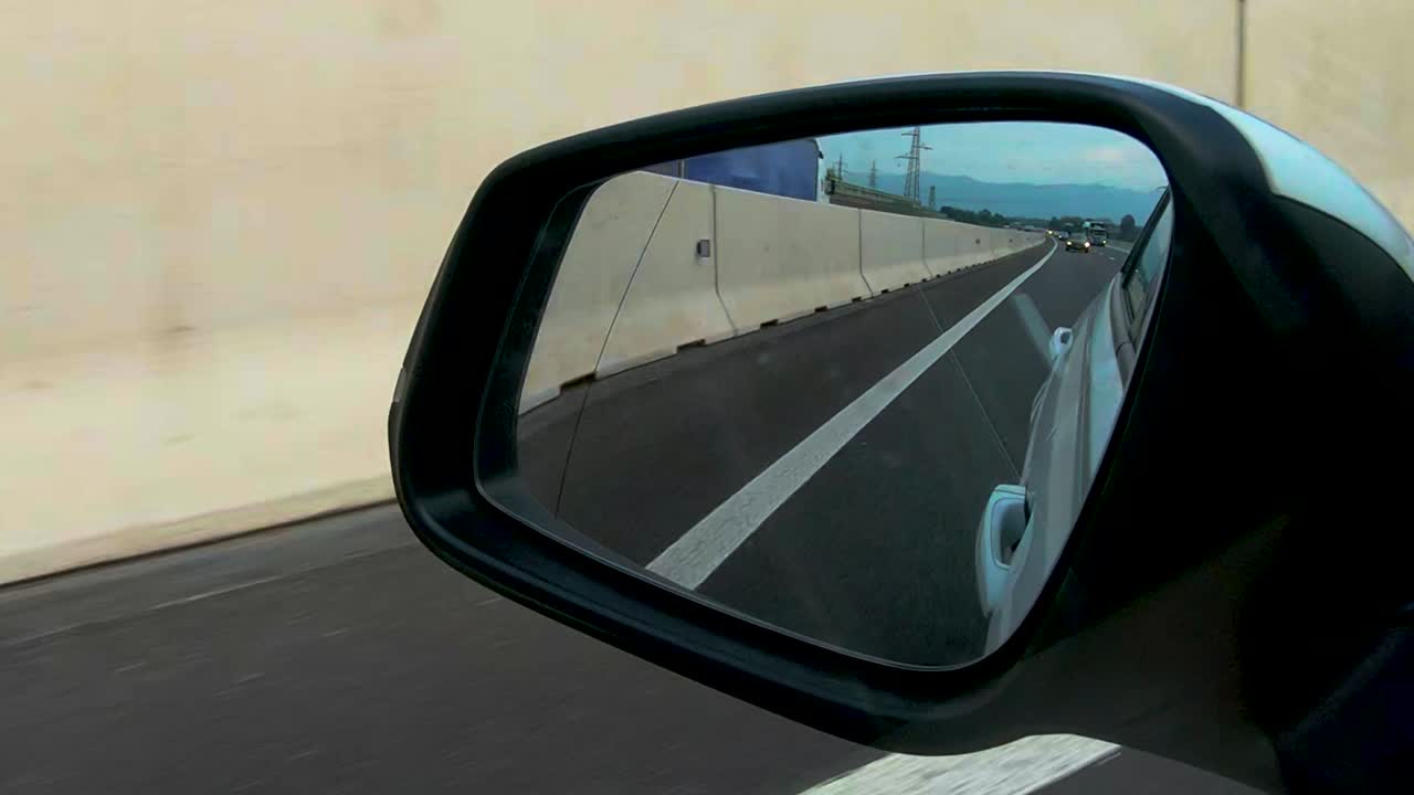 vista en el espejo retrovisor del automóvil en la autopista, transporte personal, conducción de automóviles en la autopista a lo largo de la pared de hormigón