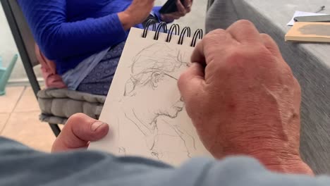 male artist sketches woman's face on notepad with pencil in garden