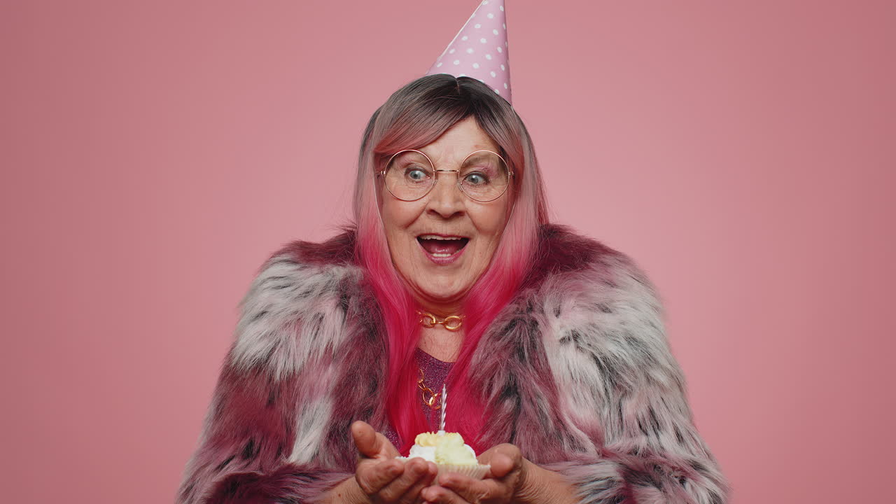 Happy senior old woman celebrating birthday anniversary party blowing candle on cake, making a wish