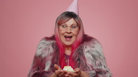 happy senior old woman celebrating birthday anniversary party blowing candle on cake, making a wish