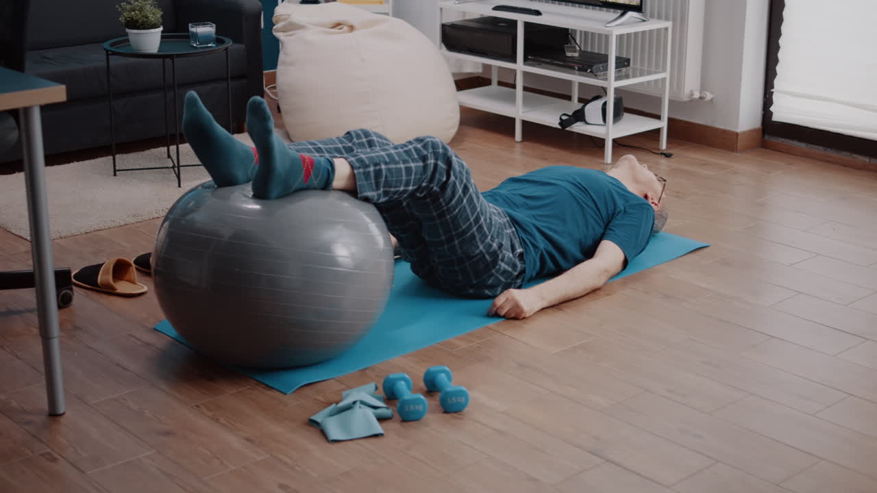 Aged person using toning ball to stretch legs muscles on yoga mat
