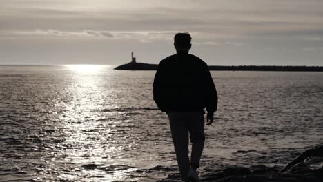 il ragazzo sta camminando sugli scogli nel mare la sera