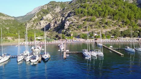aerial view of cifltik bay,footage forward towards the beach full with sunbeds and green hills.sailboats stern-to restaurant's piers on calm sea.