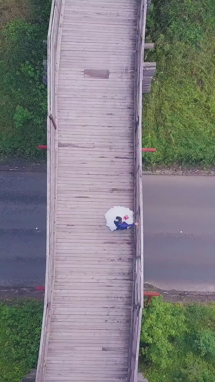 distant groom and bride on rustic wooden bridge above road and green lawn on nice sunny day upper view