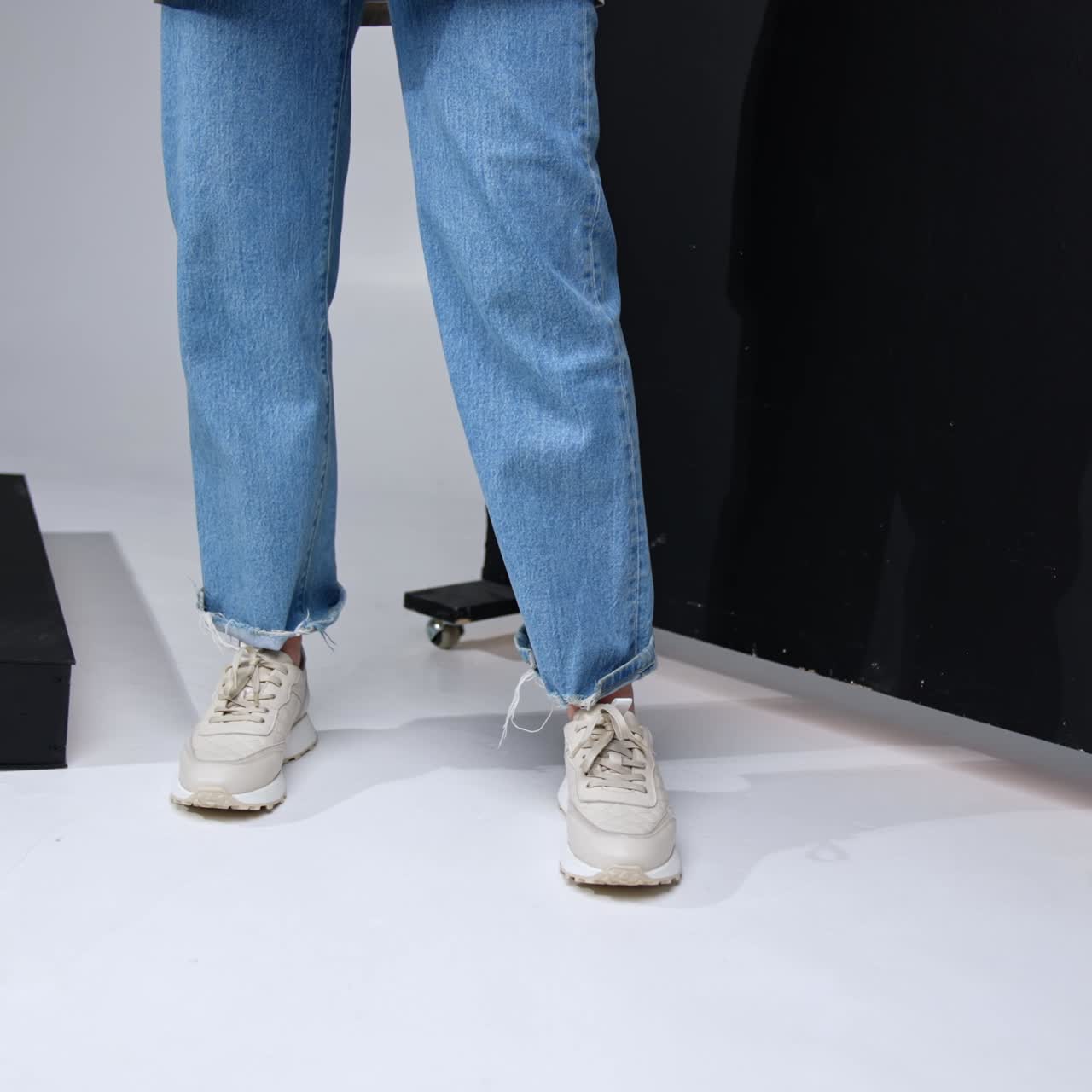 Casual modern lifestyle look. Girl in jeans and white sneakers holding a leather stylish rucksack. Black screen at backdrop
