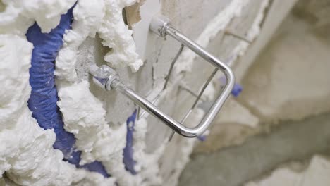 a close up shot of an exposed water pipe covered in expanding insulation foam from a shower that is currently undergoing repairs, the pipe carefully placed to avoid a stainless steel shower fitting