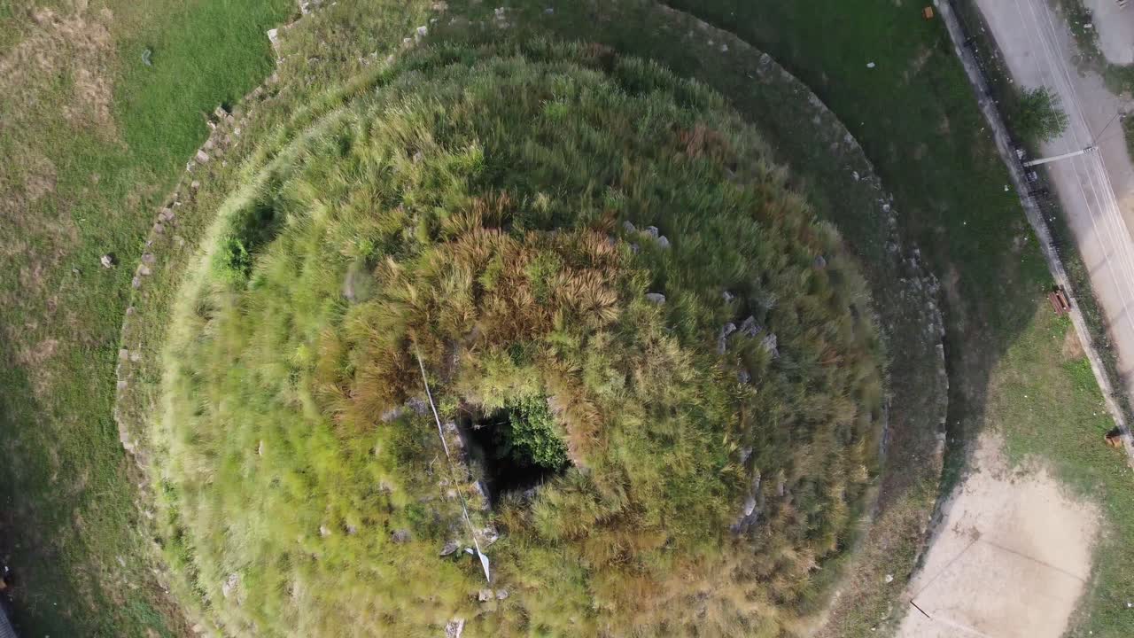 Drone view of circular grassy mound with central depression at Rani Pokhari in Butwal, Nepal, showing radial vegetation and surrounding urban area in a unique topographic pattern