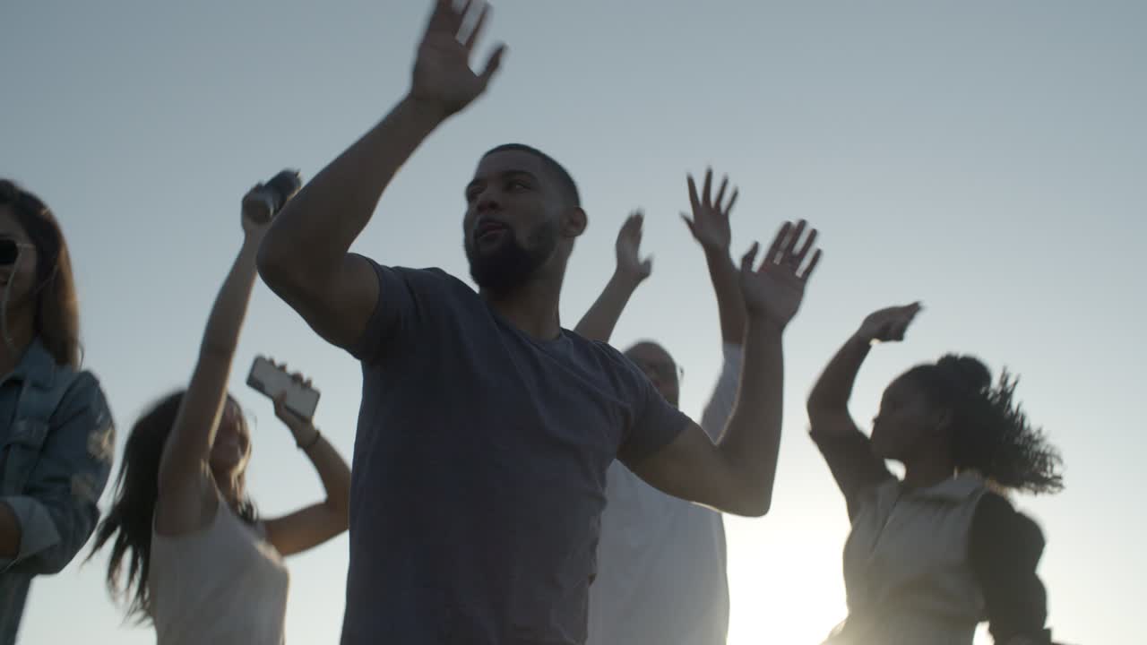 Smilende unge mennesker danser med hender i været i parken