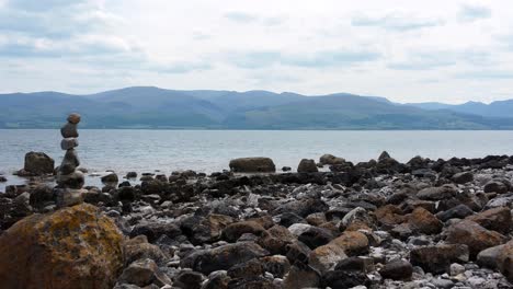 Balanced-spirituality-meditation-pebbles-piled-on-alien-rocky-mountain-range-beach-coastline-pull-back-between-towers-reveal