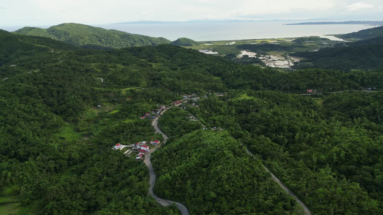 Stunning orbiting aerial view of rural hillside village amid lush tropical island greenery at Buenavista, Catanduanes, Philippines