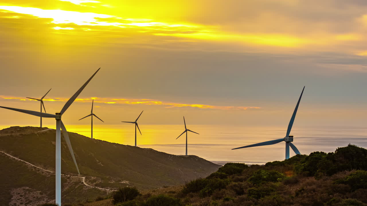 molinos de viento giratorios en primer plano paisaje panorámico, nubes al atardecer moviéndose con colinas verdes, rayos solares a través de fuentes de energía renovables