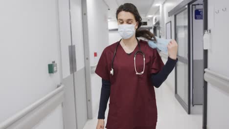 Doctora-Caucásica-Quitándose-La-Mascarilla-Y-La-Gorra-Caminando-En-El-Pasillo-Del-Hospital,-Cámara-Lenta