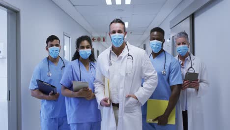 portrait of diverse group of male and female doctors in face masks standing in hospital corridor