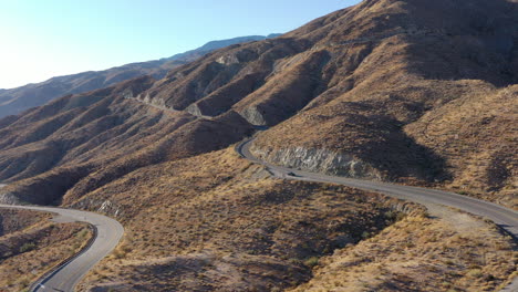 Drone-shot-of-cars-traveling-on-hairpin-curve-of-road-winding-through-barren,-rocky-mountains