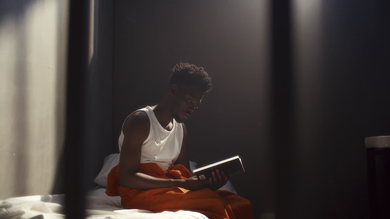 African American Inmate Sitting Alone in Prison Cell and Reading Book