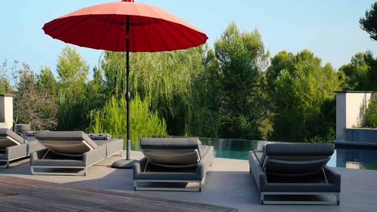 Inquadratura orbitante lenta di lettini prendisole e un ombrellone presso la piscina privata di una villa