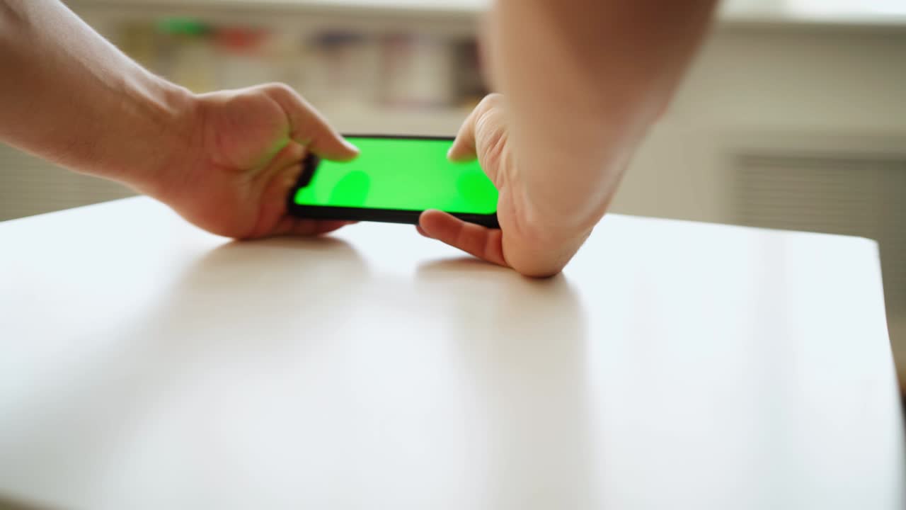 Primo piano, un uomo usa lo smartphone con schermo verde mentre è in piedi al tavolo