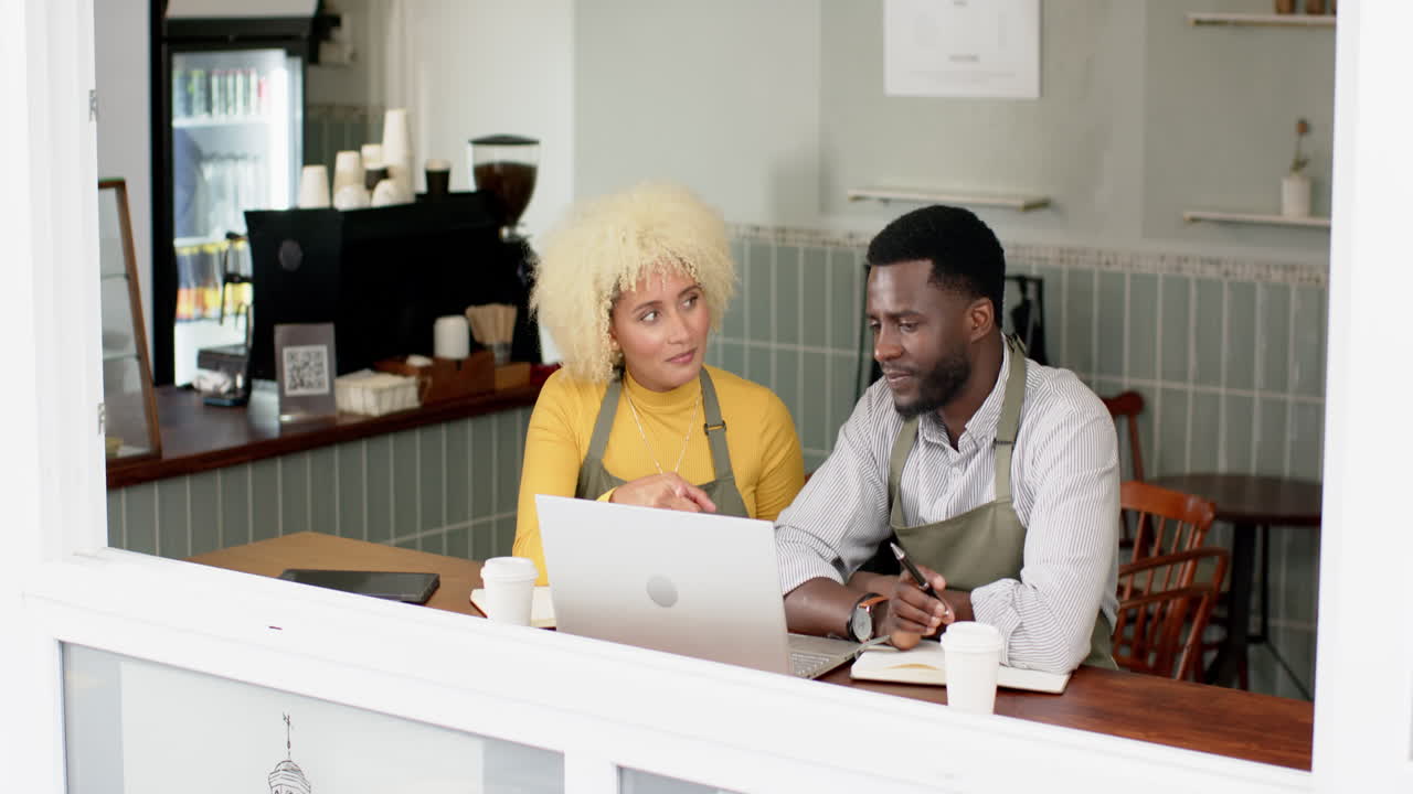 A young African American man and biracial woman talk over a laptop in a cafe