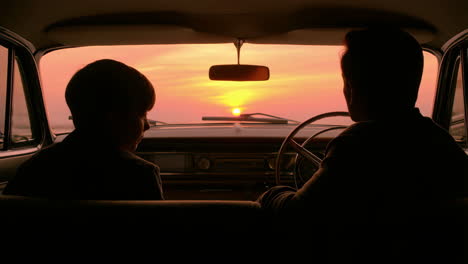 silhouetted figures in car watching sunset