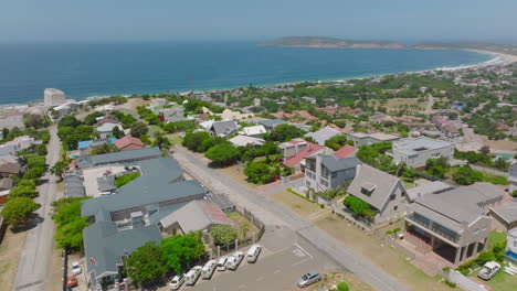 Forwards-fly-above-buildings-and-streets-in-residential-urban-borough.-Panoramic-view-of-sea-bay.-Plettenberg-Bay,-South-Africa